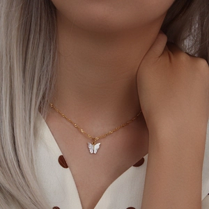 Close-up of a delicate golden butterfly necklace with a white shell pendant on model