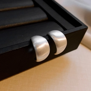 Macro view of silver matte finish C-shaped earrings on a black jewelry tray display