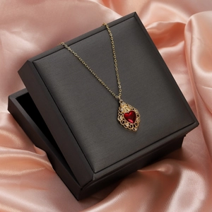 Close-up of gold heart necklace with red gemstone pendant on premium black gift box