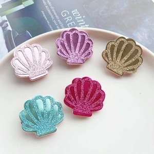 Detail of glittery shell hair accessories in pink, purple, and gold on a white plate
