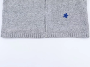 Macro detail of a gray knit cardigan with a ribbed hem and blue star applique