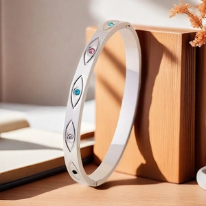 Detalle de brazalete plateado con grabados de ojos y gemas de colores sobre madera