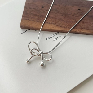 Macro shot of silver bow pendant on a delicate snake chain with polished metal finish