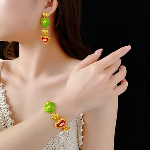Close-up of heart-shaped gold jewelry set with green and red enamel worn by a model