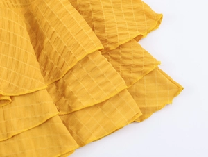 Dettaglio ravvicinato del tessuto seersucker giallo con strati a balze e motivo a quadretti