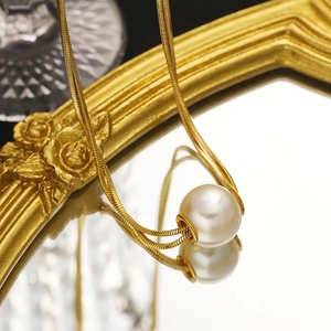 Minimalist double layer gold snake chain necklace with pearl pendant on a luxury mirror