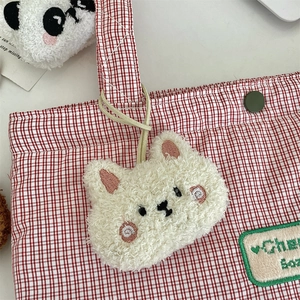 Dettaglio della borsa in tela a scacchi rossi con ciondolo peluche e toppa ricamata