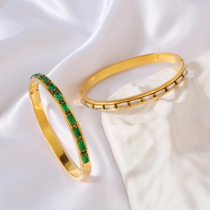 Detail of gold bracelets with emerald and white rectangular stones on silk