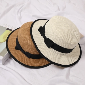 Elegant flat top straw hats in beige and brown with black ribbon bows on white fabric
