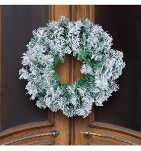 Close-up of artificial frosted Christmas wreath with snow-flocked pine needles on a wooden door