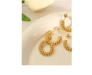 Detailed close-up of gold-plated twisted hoop earrings on a white decorative plate