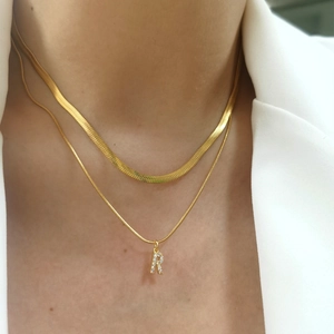 Detail of a double-layered gold snake chain necklace with an 'R' letter pendant and zircons