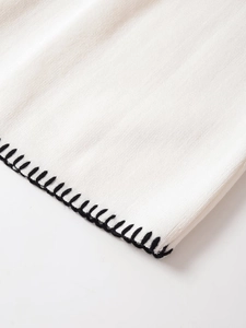 Close-up of white knit fabric texture with contrast black hand-stitched edging detail