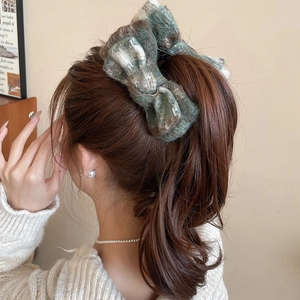 Close-up of a large checkered wool bow hair clip on long brown hair for elegant styling