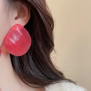 Detailed view of irregular red resin stud earring with brushed texture on model