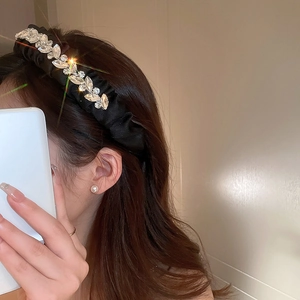Detail view of a black pleated fabric headband with leaf-shaped rhinestones and pearls