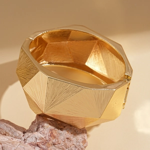 Detailansicht eines breiten goldenen Armreifs mit geometrischem Schliff und Scharnier