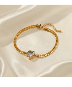 Detailed shot of golden snake chain bracelet with heart zircon on soft cream silk fabric