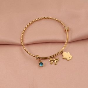 Detail of gold titanium steel bracelet with angel charm, blue gemstone and bow pendant