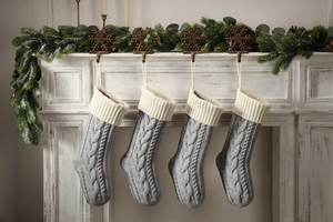 Detail of four grey cable-knit Christmas stockings with white cuffs on a mantel