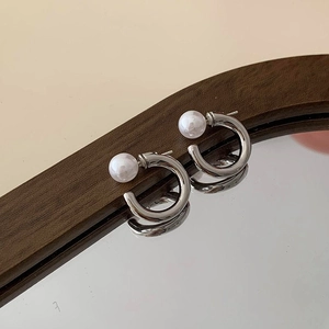 Detail showing a silver C-shaped pearl earring on a dark wood frame with mirror reflection