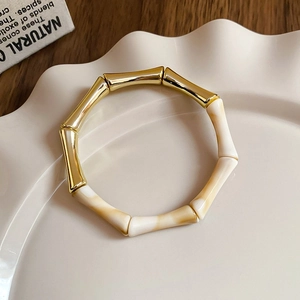 Detail of bamboo-shaped gold metal and beige marble resin bracelet on a white ceramic plate