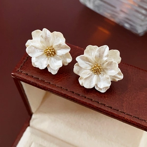 Macro detail of white pearlescent flower earrings with gold stamens on leather