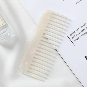 Close-up of a pearlescent white acetate wide-tooth comb on a silk and book background