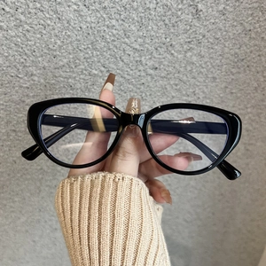 Nahaufnahme eines schwarzen Cat-Eye-Brillengestells in der Hand vor grauer Wand