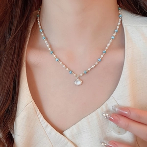 Primo piano di collana di perline blu e oro con un ciondolo bianco di forma ovale