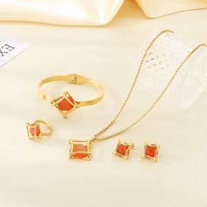 Detailed set of gold jewelry with geometric orange stones on beige soft fabric background