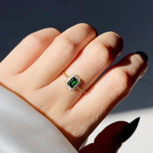 Emerald cut green stone ring with gold chain band and diamond halo on hand