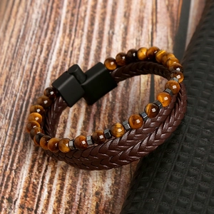 Dettaglio del cuoio intrecciato e pietre occhio di tigre sul bracciale multistrato da uomo marrone