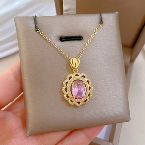 Gros plan d'un collier doré avec pendentif ovale ajouré, pierre rose et cristaux brillants