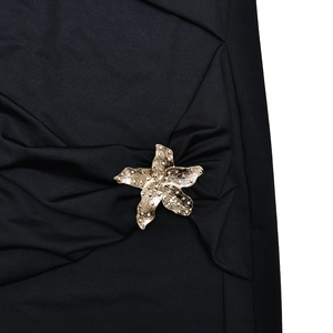Detail von schwarzem Faltenstoff mit goldenem Seestern-Metallzubehör am Kleid