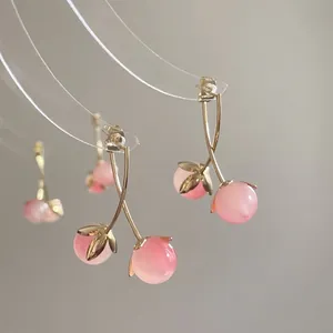 Detailed macro view of pink resin cherry earrings with golden leaf accents and stud backing
