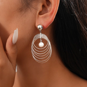 Close-up of layered silver hoop earrings with white pearls worn by a model