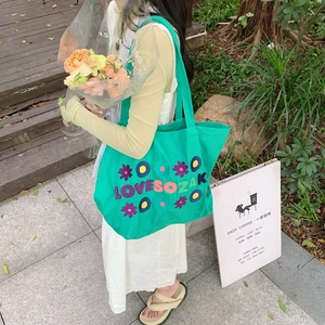 Outdoor shot of green canvas tote bag with 3D flower embroidery and LOVE SO ZAKK text