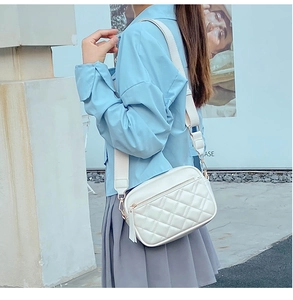 Outdoor street style view of a white quilted crossbody bag with a wide woven strap