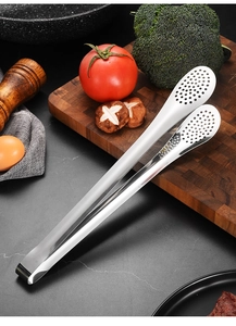 Close-up of stainless steel food tongs with perforated head on a wooden kitchen board