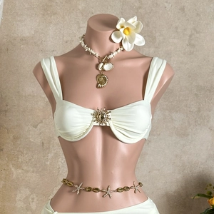 Détail du haut de bikini blanc avec boucle soleil dorée et ceinture coquillage