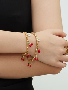 Détail de bracelets en perles dorées avec des breloques de cerise et de marguerite