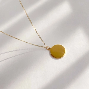 Close-up of golden sun disc pendant necklace with artistic shutter shadows on white surface