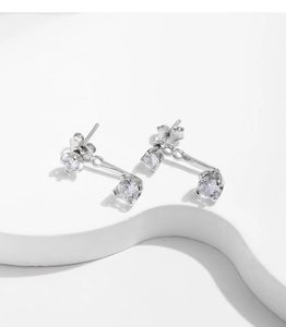 Macro shot of silver stud earrings with clear zircons on a wavy white base pedestal
