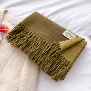 Detail view of an olive green cashmere-style scarf with soft tassels and brand label