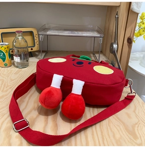 Detail view of a cute plush tomato crossbody bag with soft legs and green leaf accents