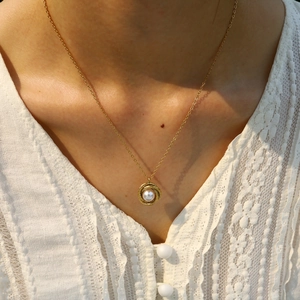 Detail of a gold-plated twisted spiral pendant with a white pearl on a delicate chain