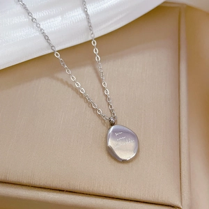 Macro shot of silver titanium steel necklace with irregular bean pendant and cursive text