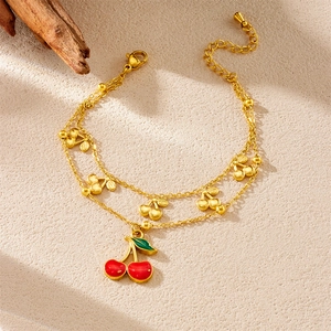 Double-layered gold chain bracelet featuring red enamel cherry charms on a beige background