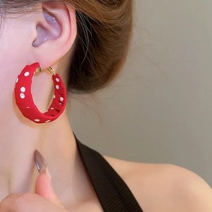 Close-up of a large red fabric hoop earring with white polka dots worn by a model